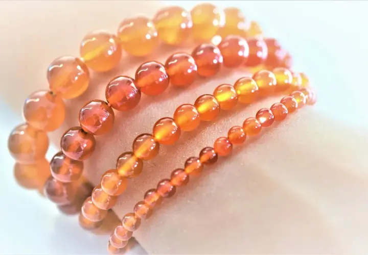 Armbänder aus leuchtenden, orange-roten Feuerachat-Kugeln in verschiedenen Größen, die wie ein warmer Sonnenuntergang auf der Haut liegen.