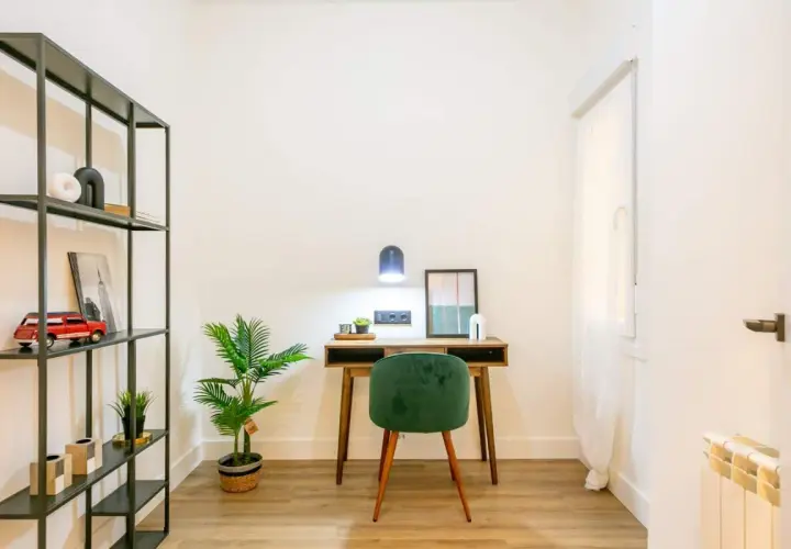 Escritorio de madera con silla verde, planta y estantería metálica. La luz de la lámpara es de 4000 K, creando un ambiente acogedor.