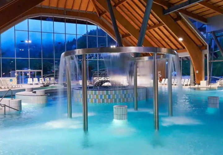 Piscina interna con cascata, lettini e vista sulle montagne. Un luogo ideale per rilassarsi nelle terme in Slovenia vicino al confine italiano.