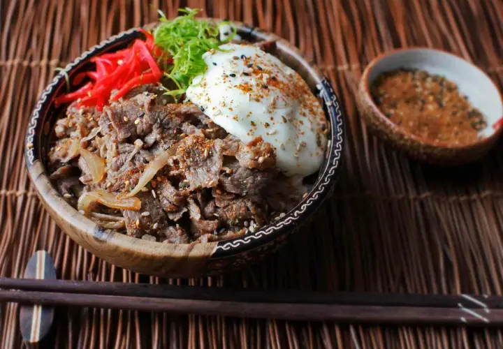 A delicious Yoshinoya beef bowl recipe, featuring tender beef, onions, a fried egg, pickled ginger, and green onions, ready to be enjoyed.