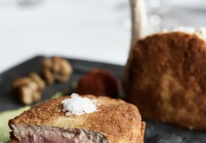 Ein knuspriges Kalbsschnitzel, italienisch zubereitet, mit feinen Beilagen auf einem dunklen Teller.