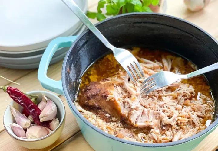 Szarpana wieprzowina w garnku, rozrywana widelcami, obok czosnek i papryczka chili.
