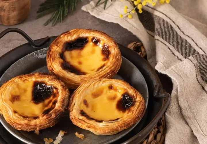 Trois délicieux flans portugais, dorés et caramélisés, sur un plateau en métal.