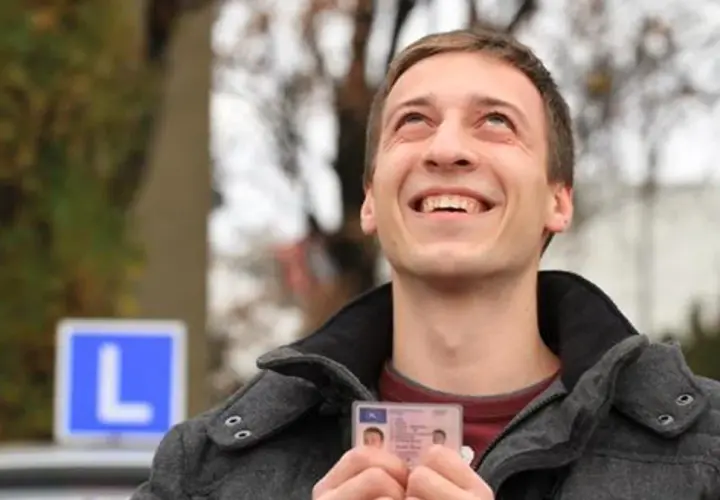 Szczęśliwy młody mężczyzna trzyma prawo jazdy, sprawdzając czy jest do odbioru. W tle niebieski znak "L".
