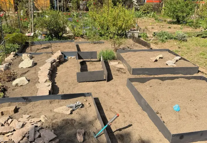 Gartenanlage mit Hochbeeten und naturnahen Gartenwegen aus Steinen. Werkzeuge liegen bereit.