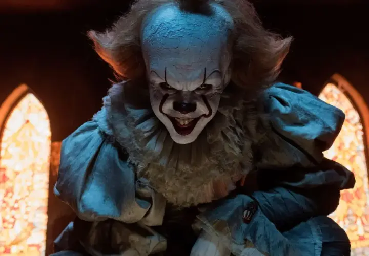 Gripsou le clown dansant, au sourire terrifiant, se tient dans une église sombre, ses yeux brillants fixant l'objectif.