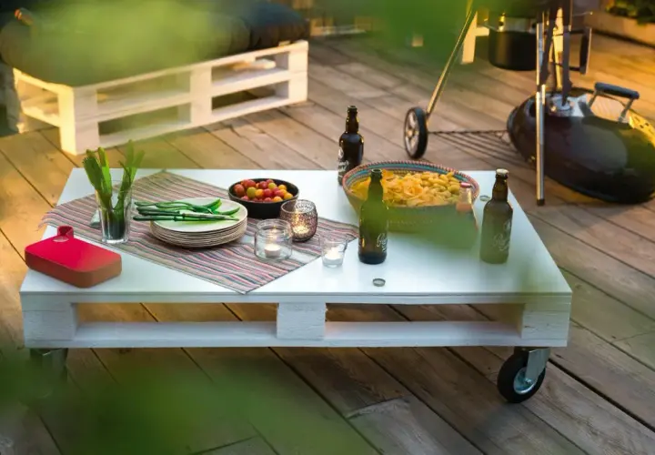 Tavolo fai da te con snack, bevande e candele su un deck di legno, pronto per una grigliata.