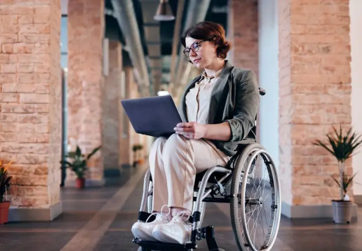 Kobieta na wózku inwalidzkim pracuje na laptopie. Czy lekarz rodzinny może wystawić zlecenie na wózek inwalidzki?