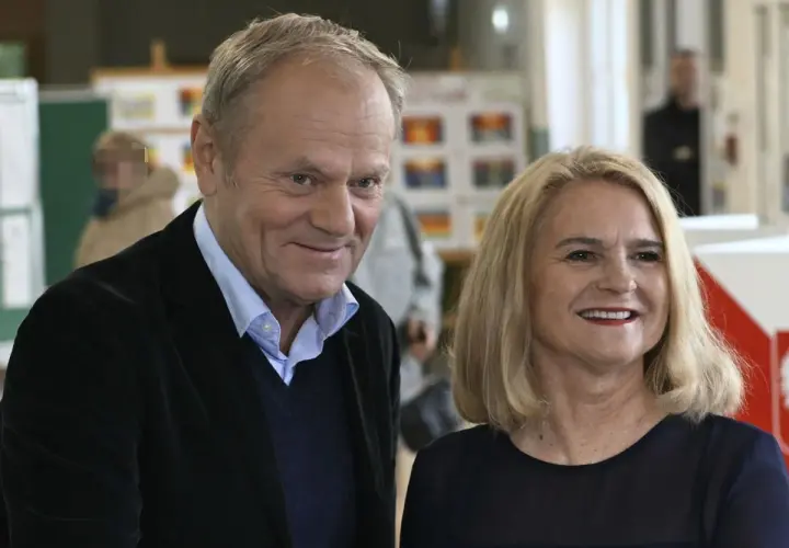 Donald Tusk z żoną, uśmiechnięci, w tle wyborcze plakaty.
