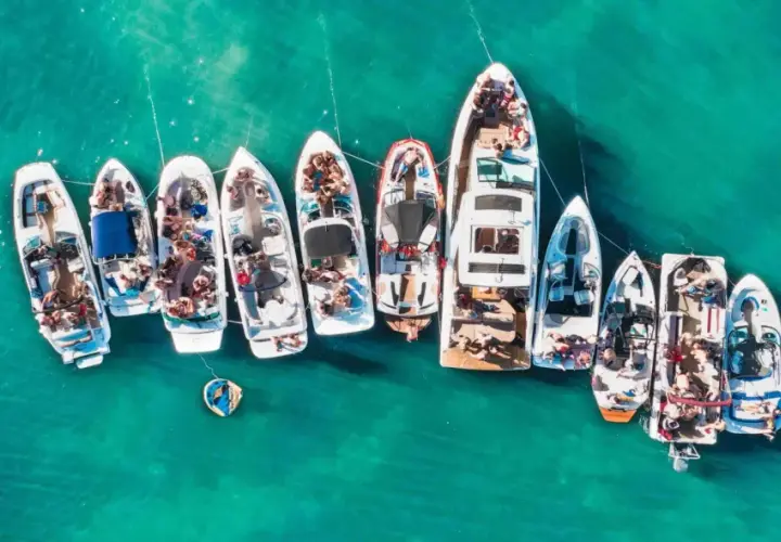 Grupa łodzi cumuje blisko siebie na turkusowej wodzie, tworząc wrażenie wodnego festiwalu. To idealny prom majorka ibiza dla miłośników słońca i zabawy na morzu.