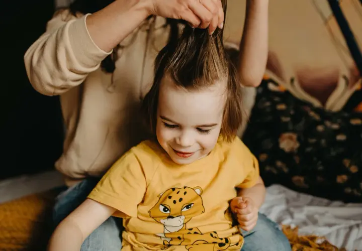 Mama delikatnie rozczesuje kołtuny u dziecka, które uśmiecha się, patrząc w dół.