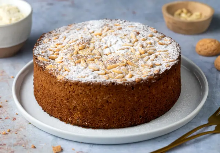 Torta rustica con farina di mandorle, cosparsa di zucchero a velo e pinoli tostati. Un dolce invitante, perfetto per ogni occasione.