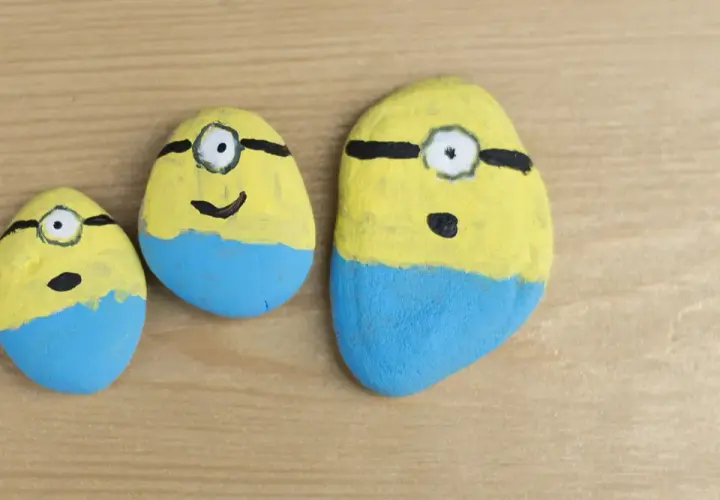 Trzy kamienie polne pomalowane na żółto i niebiesko, przypominające Minionki. Zabawne malowanie kamieni polnych.