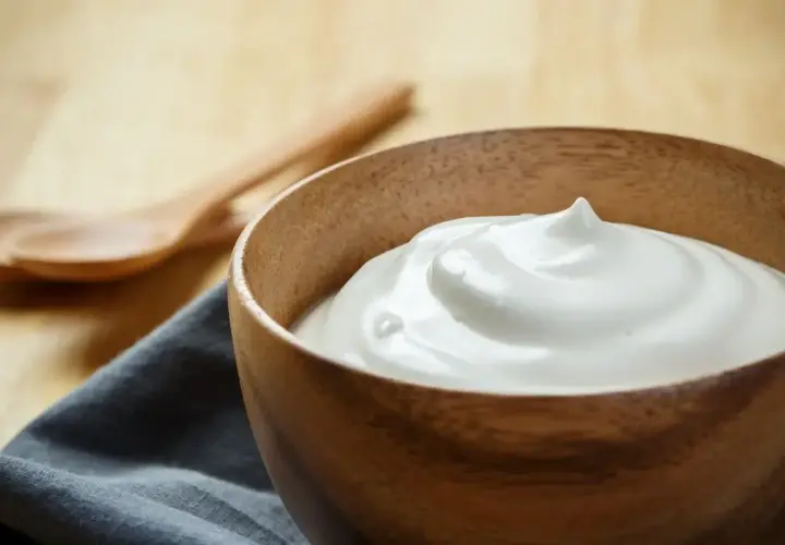 Una ciotola di legno contiene una soffice crema al latte, pronta per essere gustata. Due cucchiai di legno sono sullo sfondo.