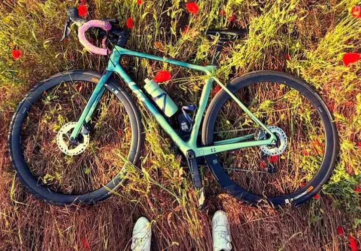 Zielony rower leżący na łące pełnej maków, z widocznymi butami rowerowymi.