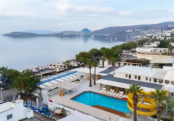 Widok na basen i plażę z leżakami. W tle morze i zabudowania. Idealne miejsce na wakacje, jak sugerują petunya beach resort opinie.