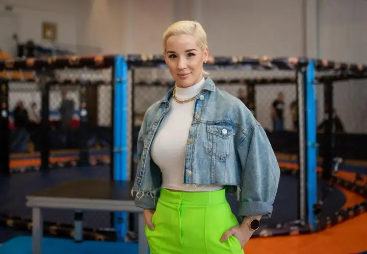 Kobieta w dżinsowej kurtce i neonowych spodniach stoi przed klatką MMA. Ile lat ma Aniela Bogusz?
