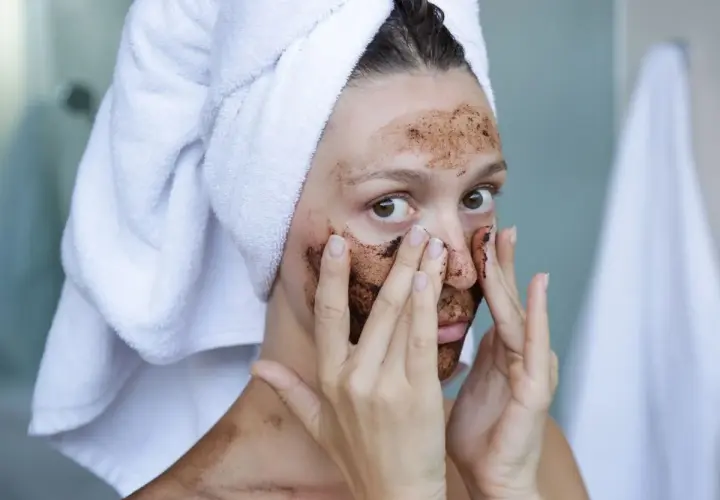 Kobieta z ręcznikiem na głowie nakłada na twarz domowy peeling złuszczający do twarzy.