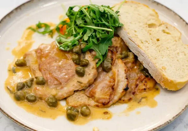 Pyszne saltimbocca alla romana z cielęciną, szynką, szałwią i kaparami w sosie, podane z rukolą i chlebem.