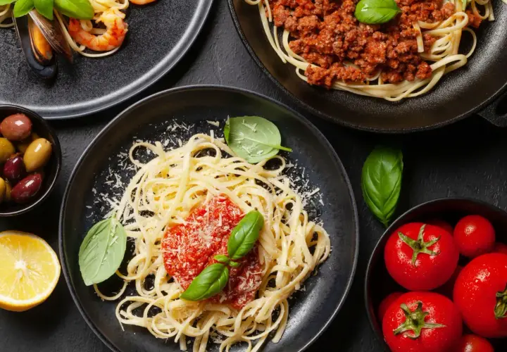 Pyszne spaghetti z sosem pomidorowym i bazylią, posypane czymś, co świetnie sprawdzi się co zamiast parmezanu. Obok talerz z owocami morza i mięsem mielonym.