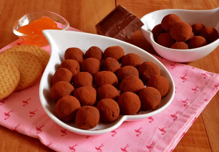 Bon bon cioccolato e panna anni '80, un dolce ricordo. Praline al cacao su un piatto bianco, con biscotti e marmellata d'arancia.