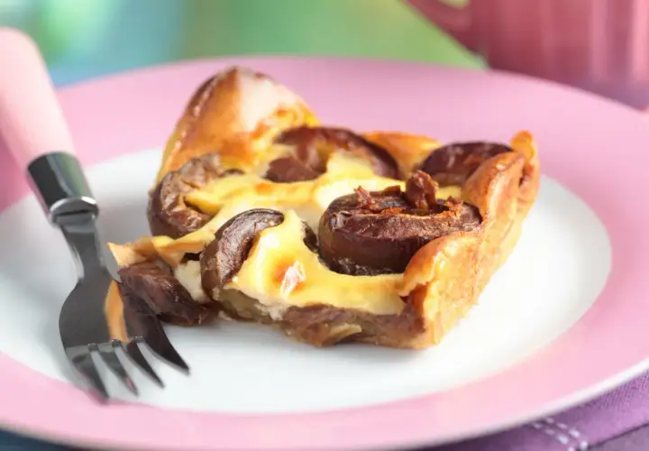 Tranche de clafoutis aux prunes moelleux sur une assiette rose avec une fourchette.