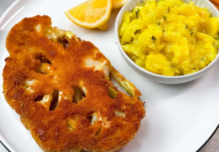 Knuspriges Blumenkohl-Schnitzel mit Kartoffelsalat und Zitronenspalten auf einem weißen Teller.
