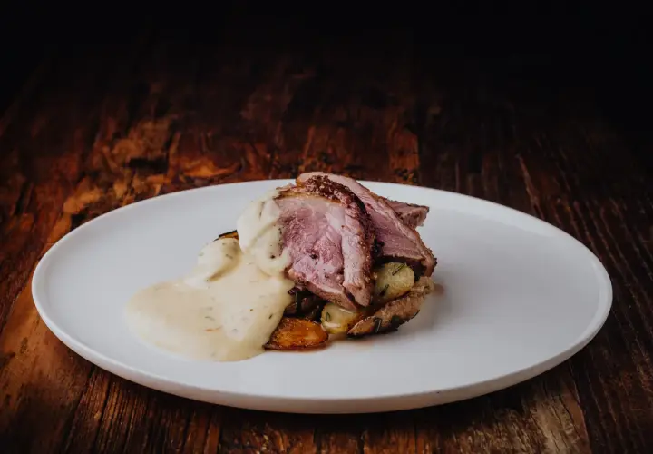 Tranches de gigot d'agneau au four, nappées d'une sauce crémeuse, servies sur des pommes de terre rôties. Un délice visuel et gustatif.