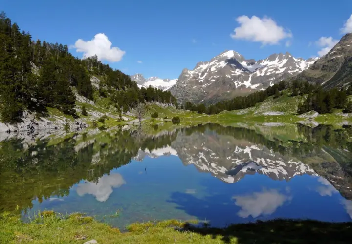 Espejo de agua en los valles de Huesca, reflejando montañas nevadas y un cielo azul con nubes.