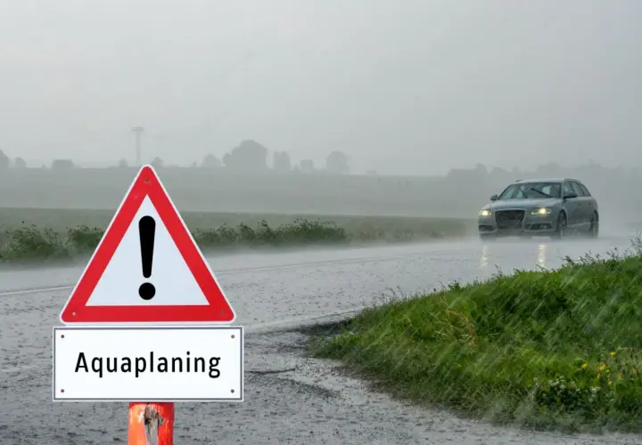 Señal de advertencia de aquaplaning en un día lluvioso. Un coche circula por la carretera mojada. ¿Qué puede hacer para evitar el aquaplaning?
