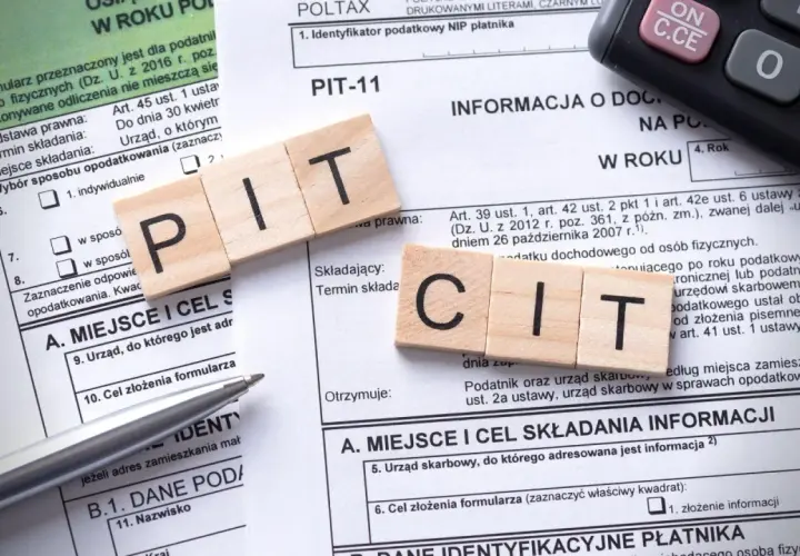 Drewniane klocki z literami PIT i CIT leżą na formularzach podatkowych. Temat: podatek od sprzedaży nieruchomości po upływie 5 lat.