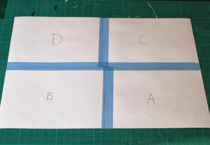 Papier divisé en quatre sections (A, B, C, D) par du ruban adhésif bleu rayé, prêt à créer un motif.