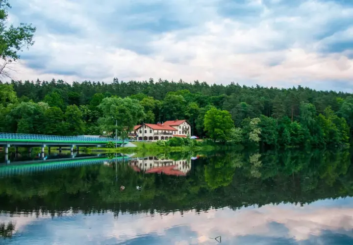 Malowniczy hotel nad jeziorem, z mostem i lasem w tle. Idealne miejsce na rodzinne wakacje, oferujące atrakcje dla dzieci.