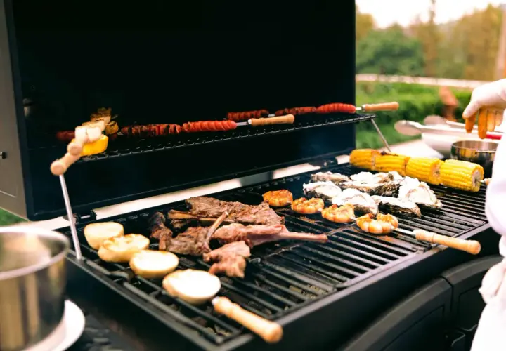 Viande, crevettes, huîtres et maïs grillés sur un barbecue gaz ou charbon. Des saucisses enroulées cuisent sur la grille supérieure.