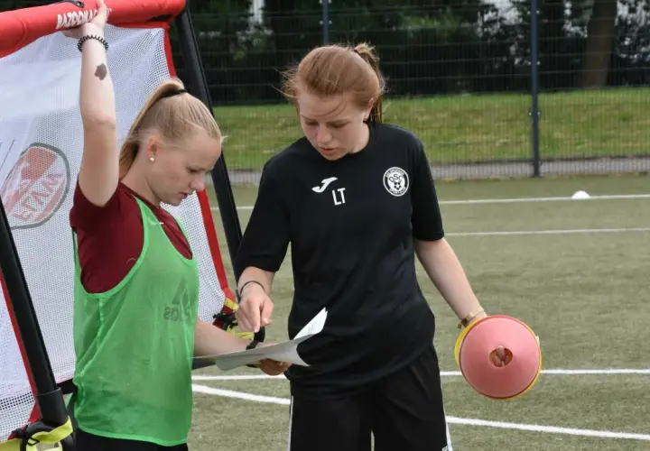 Zwei junge Fußballerinnen besprechen den Trainingsplan. Die eine hält einen Zettel, die andere einen Trainingskegel. Perfekte f jugend spielzeit.