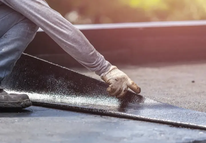 Hand mit Handschuh legt neue Dachpappe an. Alte Dachpappe entsorgen ist wichtig für die Langlebigkeit.