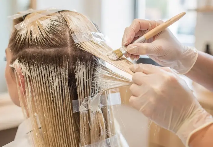 Manos enguantadas aplican tinte para crear mechas blancas en cabello rubio.