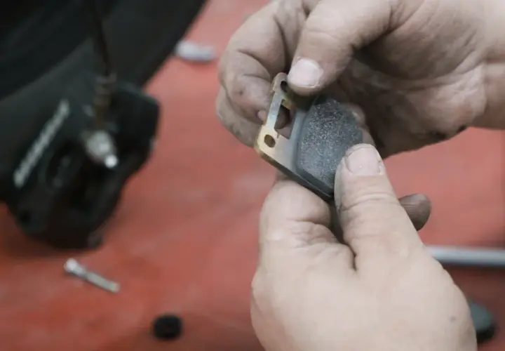 Manos sucias sostienen una pastilla de freno de moto lista para el cambio.