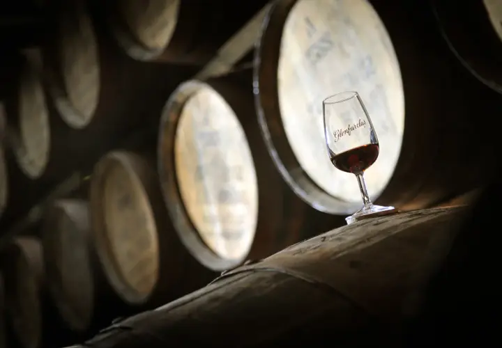 Kieliszek whisky Glenfarclas na beczce, symbol najlepszych technik leżakowania whisky finiszowanie w beczkach po sherry.