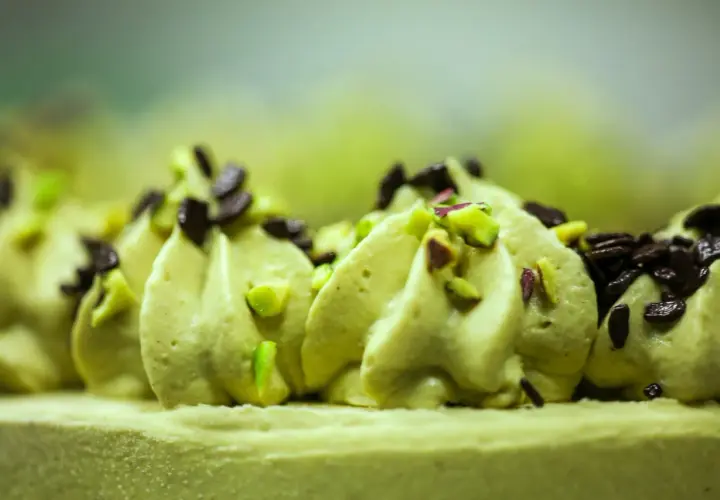 Puszysty krem pistacjowy do tortu, ozdobiony kawałkami pistacji i czekolady.