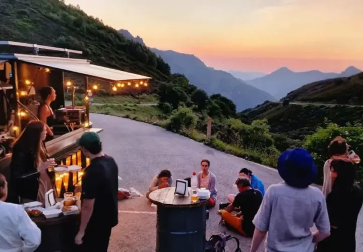 Gente disfrutando de comida y bebida en un food truck con vistas a montañas al atardecer. Un lugar ideal para descubrir los mejores pueblos para comer en Asturias.