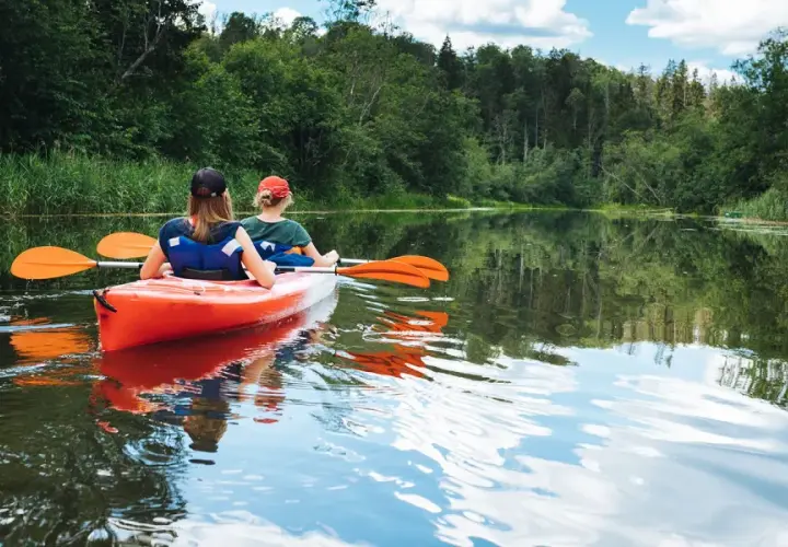 Dwie osoby płyną kajakiem po spokojnej rzece, otoczonej zielenią. Idealne miejsce na spływ kajakowy Mazury, gdzie najlepiej poczuć bliskość natury.