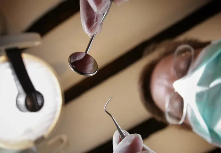 Dentysta w masce i rękawiczkach trzyma narzędzia. Zastanawiasz się, ile kosztuje znieczulenie u dentysty?