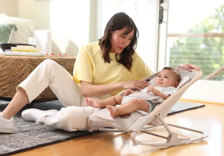 En kvinna sitter på golvet bredvid en bebis i en babysitter från Maxi-Cosi.