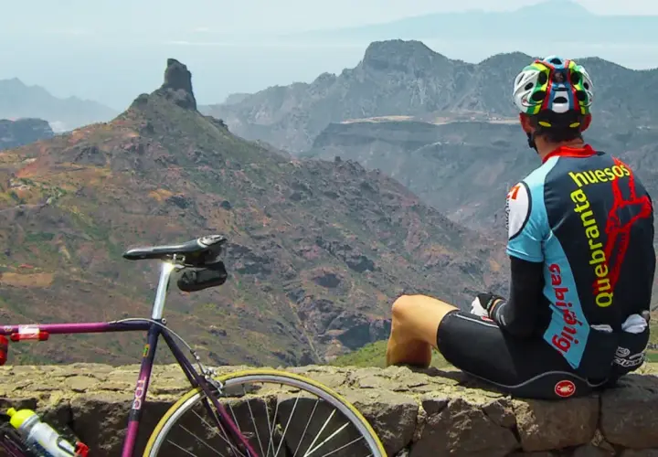 Ciclista descansa tras explorar rutas en bici Gran Canaria. Paisaje montañoso y su bicicleta morada.