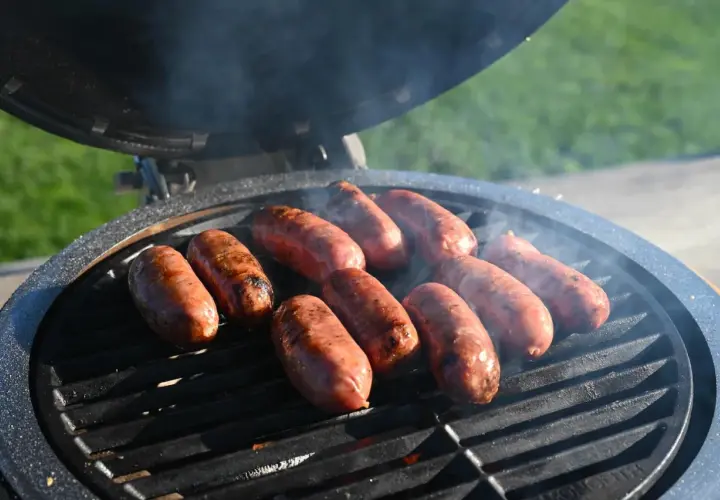 Mehrere Salsiccia brutzeln auf einem Grill. Rauch steigt auf und die Würste bekommen schöne Grillstreifen.