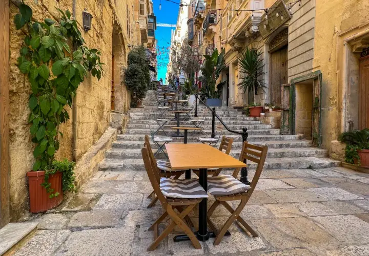 Malta sierpień: kamienne schody i stoliki kawiarniane w wąskiej uliczce, idealne na letni wieczór.