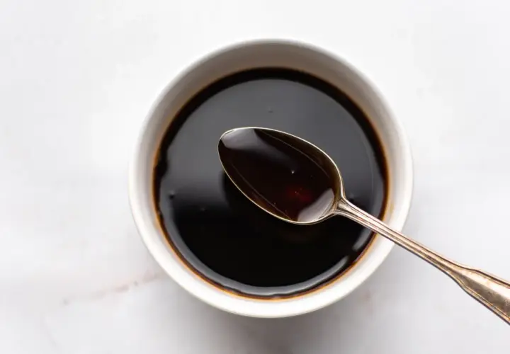 A spoon rests in a bowl of dark liquid, hinting at how to make sweet soy sauce.