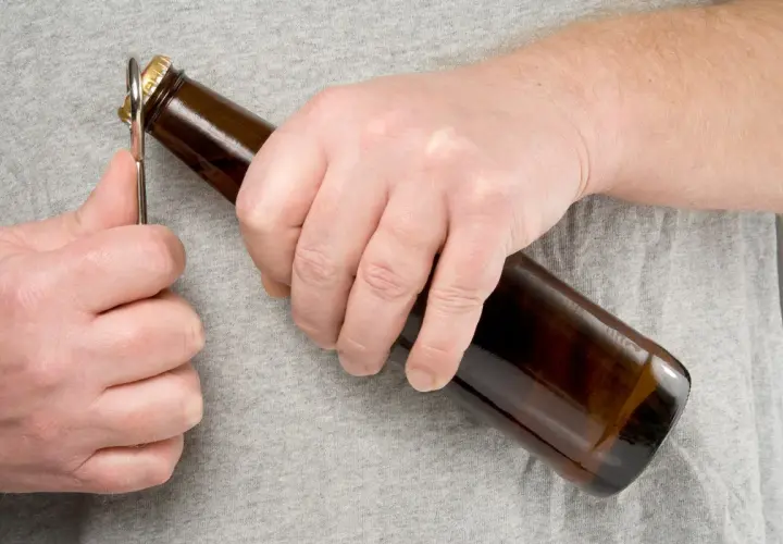Main gauche ouvrant une bouteille de bière avec un décapsuleur. L'embouteillage bière est imminent.