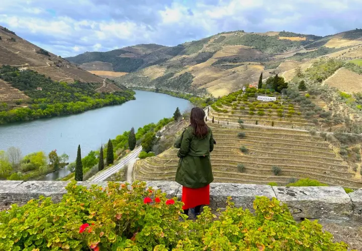 Mujer admira el hermoso **recorrido del Duero** desde un mirador, con viñedos en terrazas y el río serpenteando entre colinas verdes.